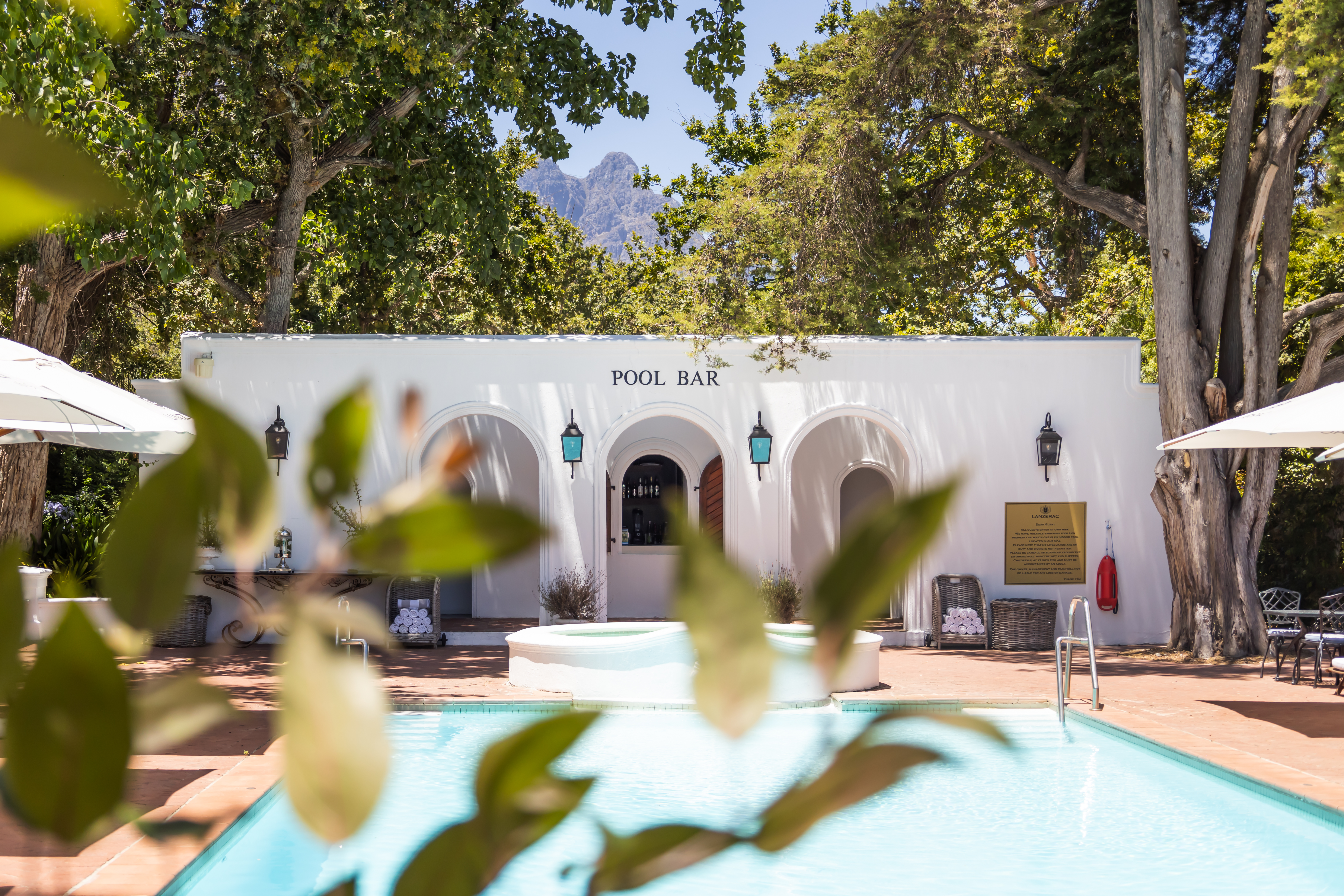 Pool bar and swimming pool at Lanzerac estate in Stellenbosch surrounded by trees with the Jonkershoek Mountains visible in South Africa’s Cape Winelands.