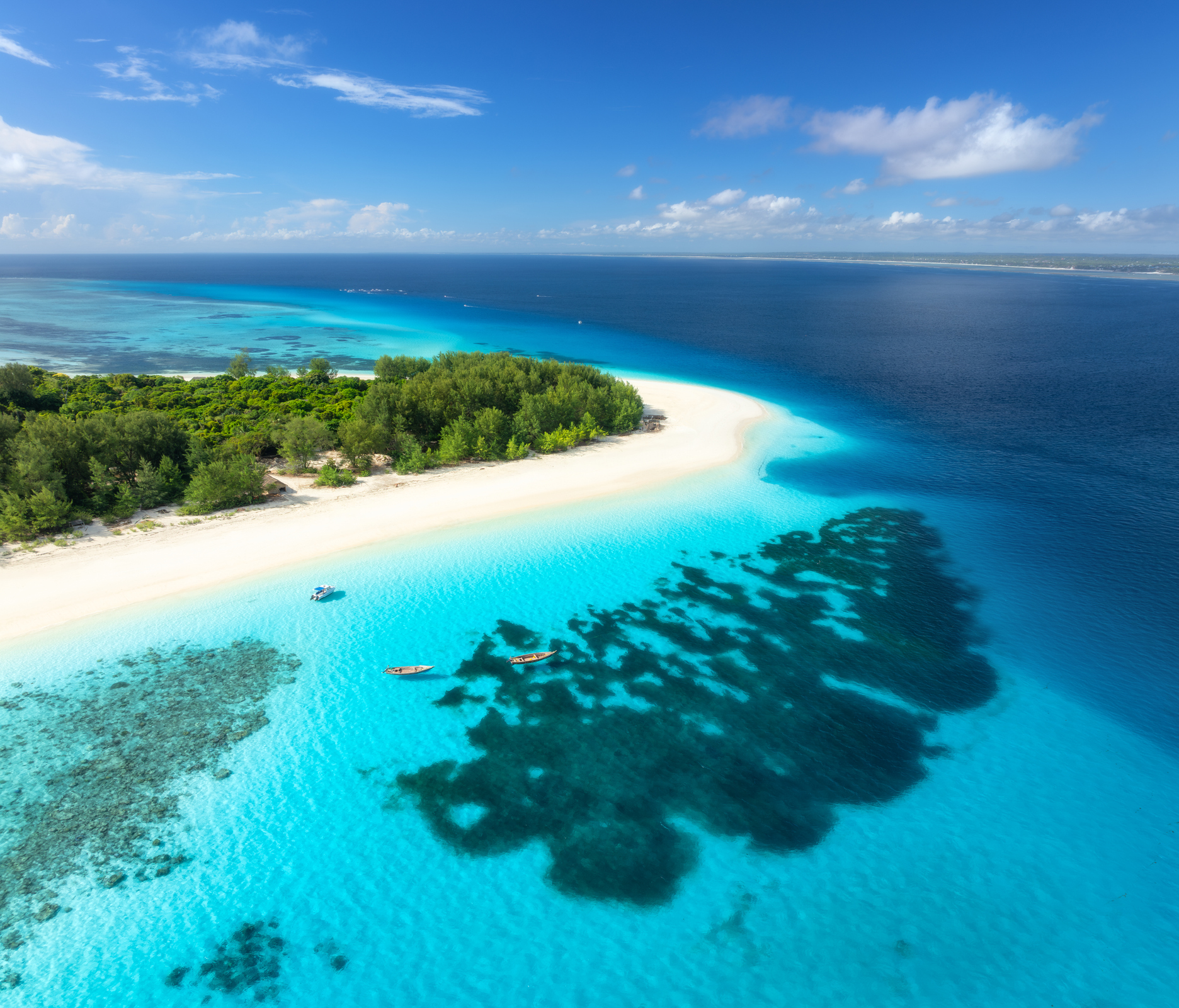 Aerial view of Mnemba Island showing white sand beaches, turquoise lagoon, coral reefs, and the Indian Ocean off Zanzibar, Tanzania.
