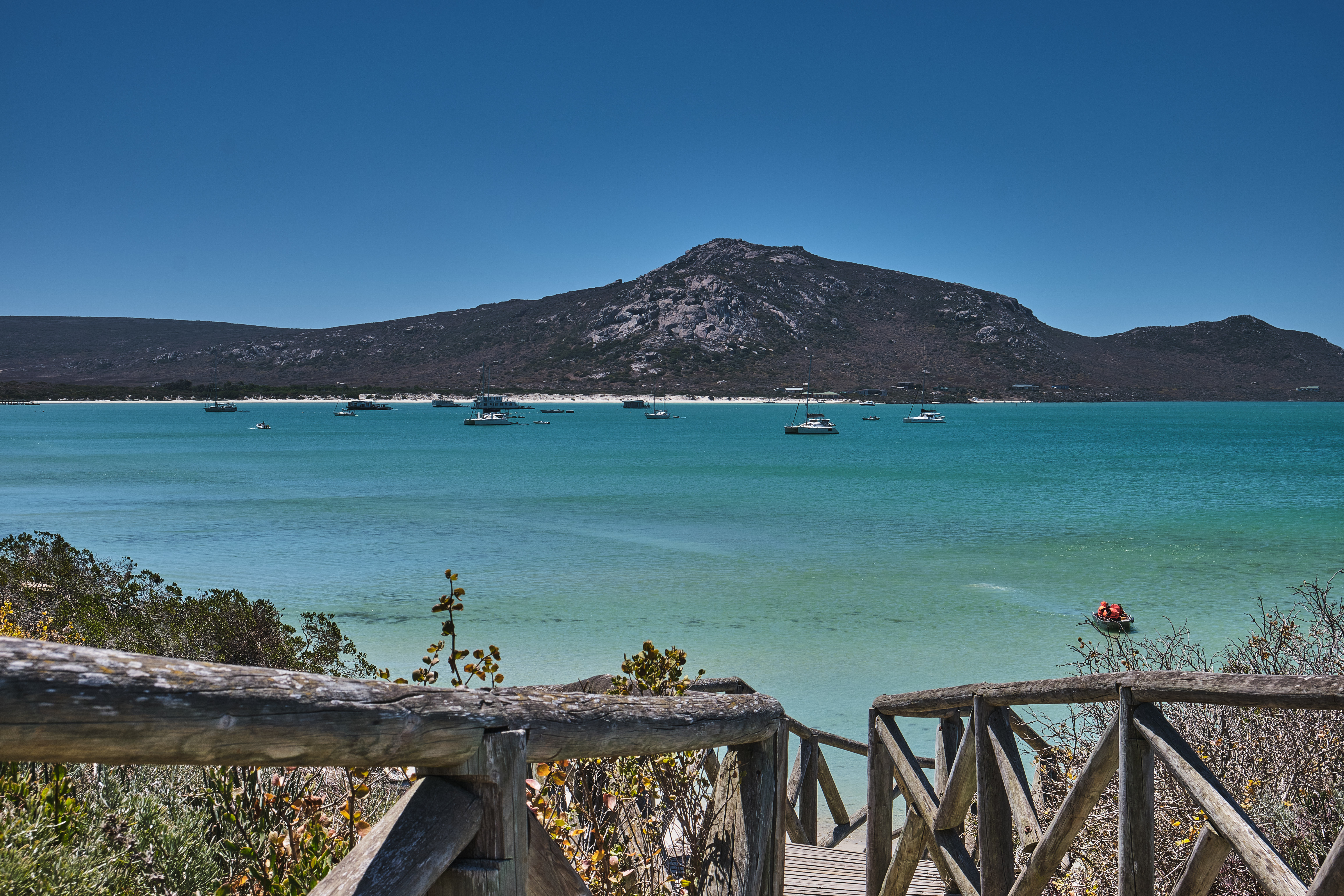 View across the turquoise waters of Langebaan Lagoon with anchored sailboats and coastal hills in the background, Western Cape, South Africa.
