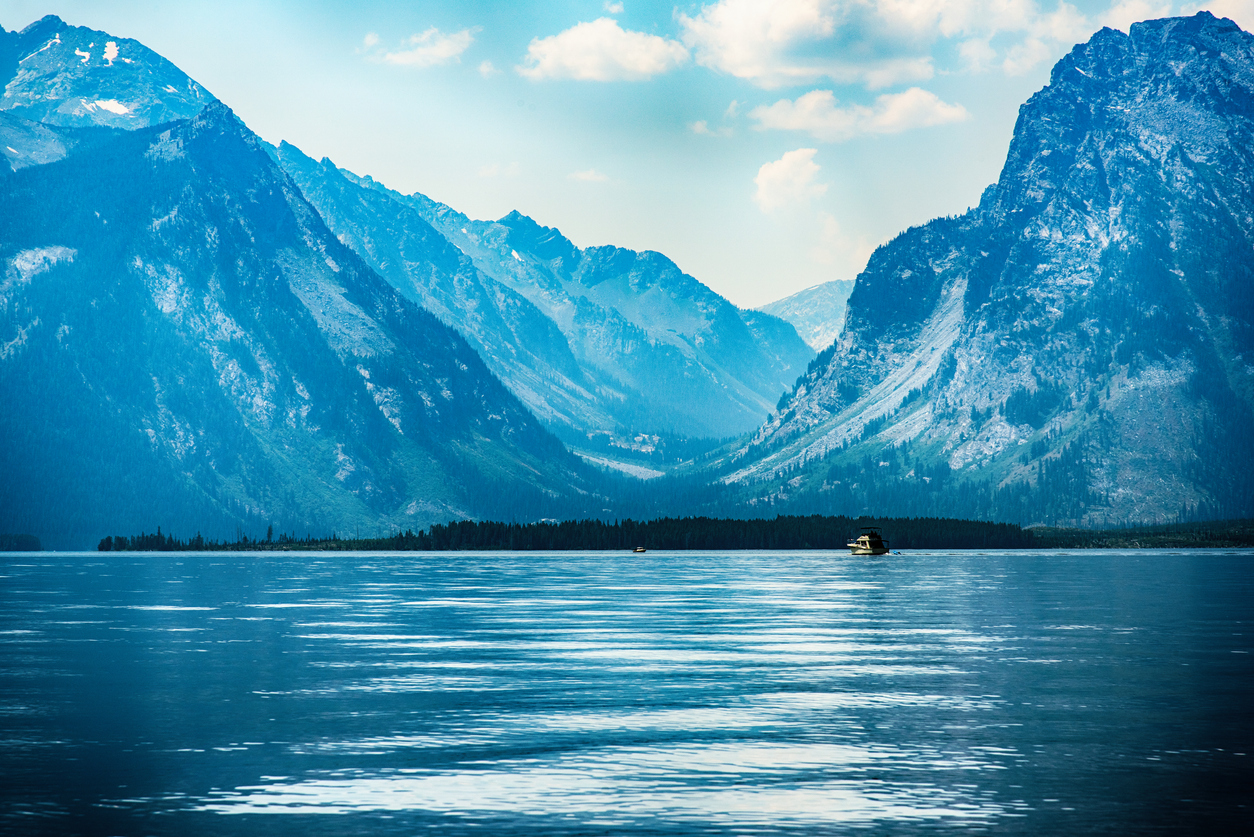 Single boat on Jackson Lake with layered Teton Range mountains in Grand Teton National Park, Wyoming, USA.