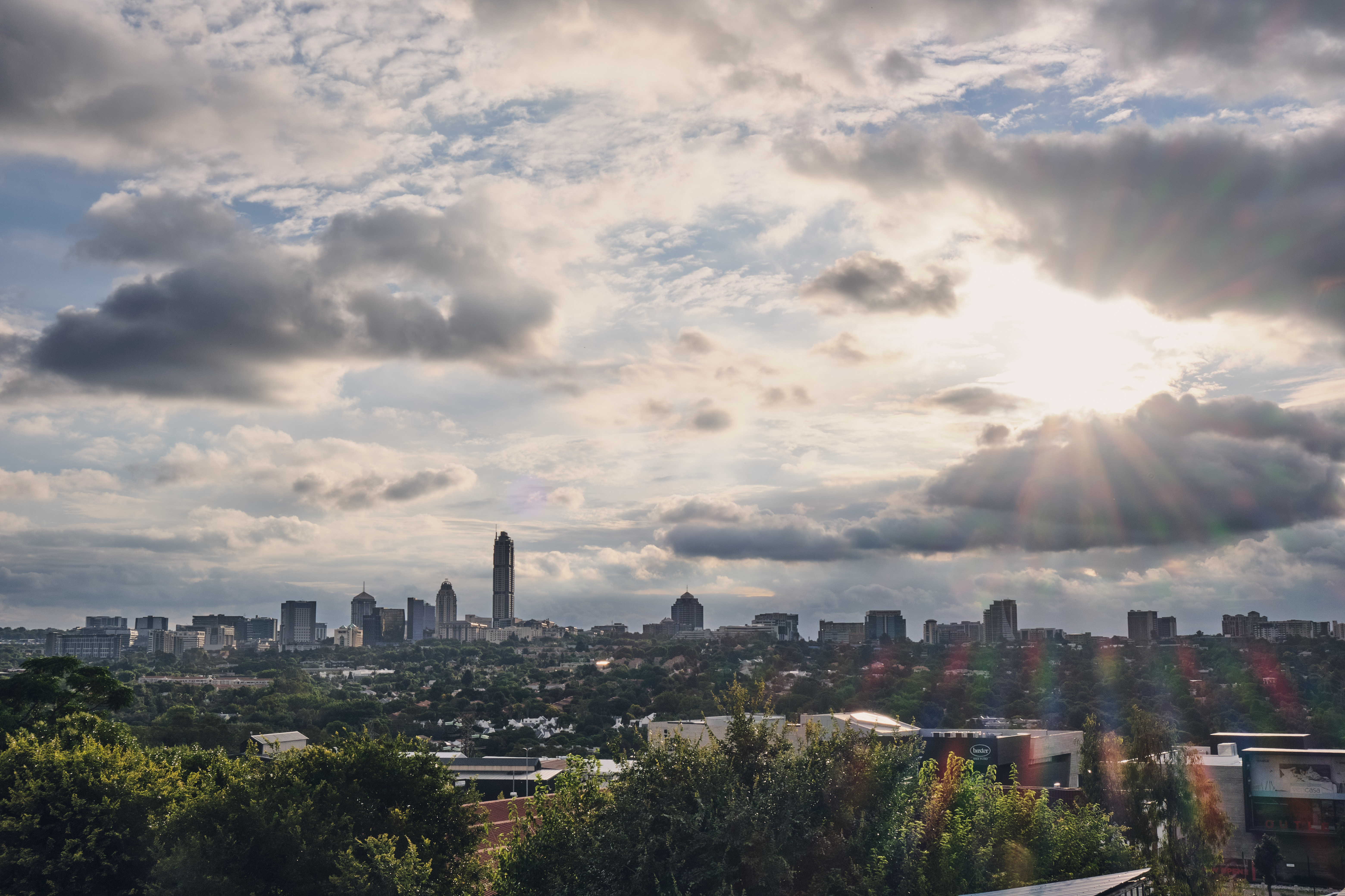 Sandton skyline in Johannesburg, South Africa, with The Leonardo tower rising above the city as sunlight streams through dramatic storm clouds.