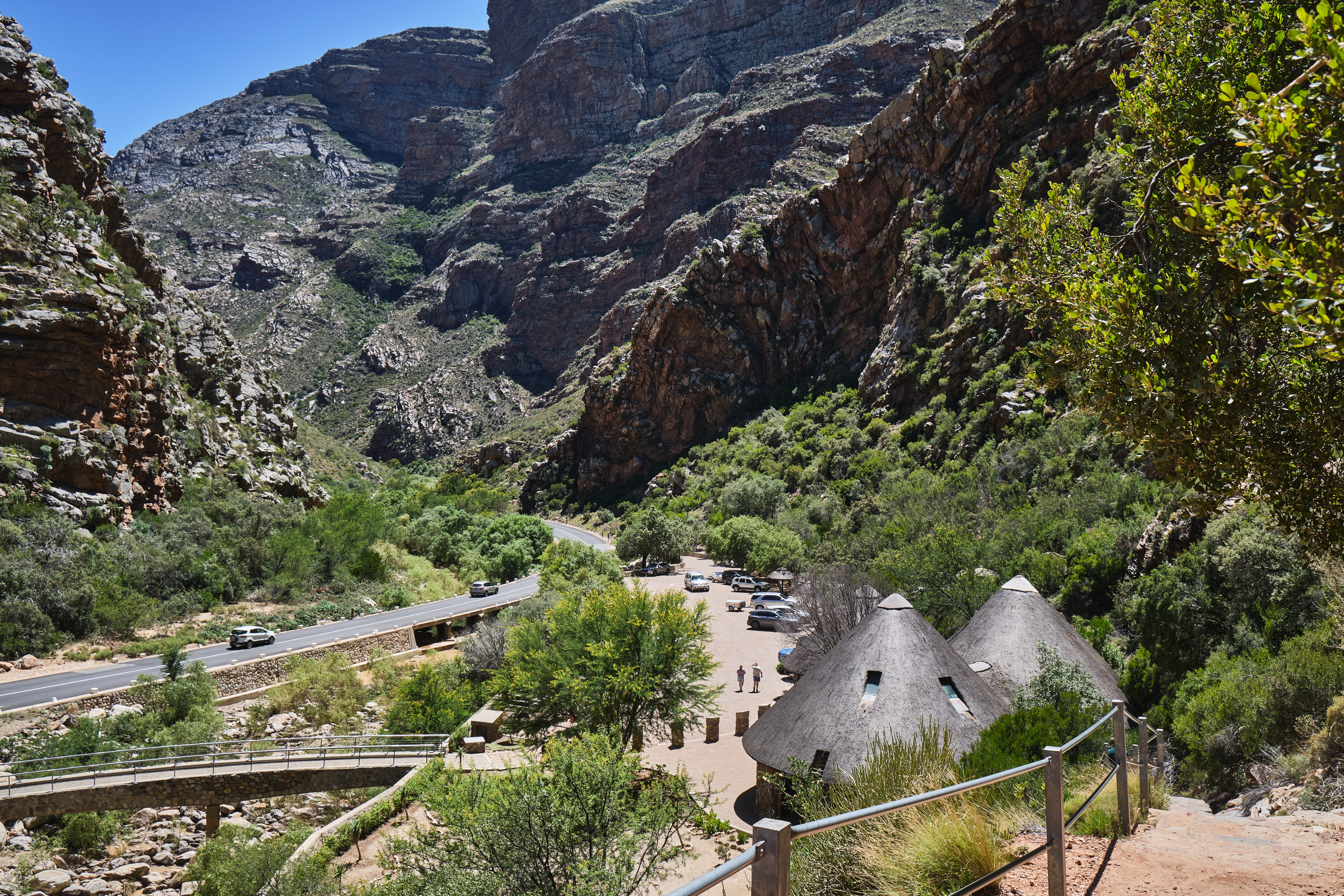 Road, visitor area, and steep sandstone canyon walls within Meiringspoort in the Western Cape region of South Africa.
