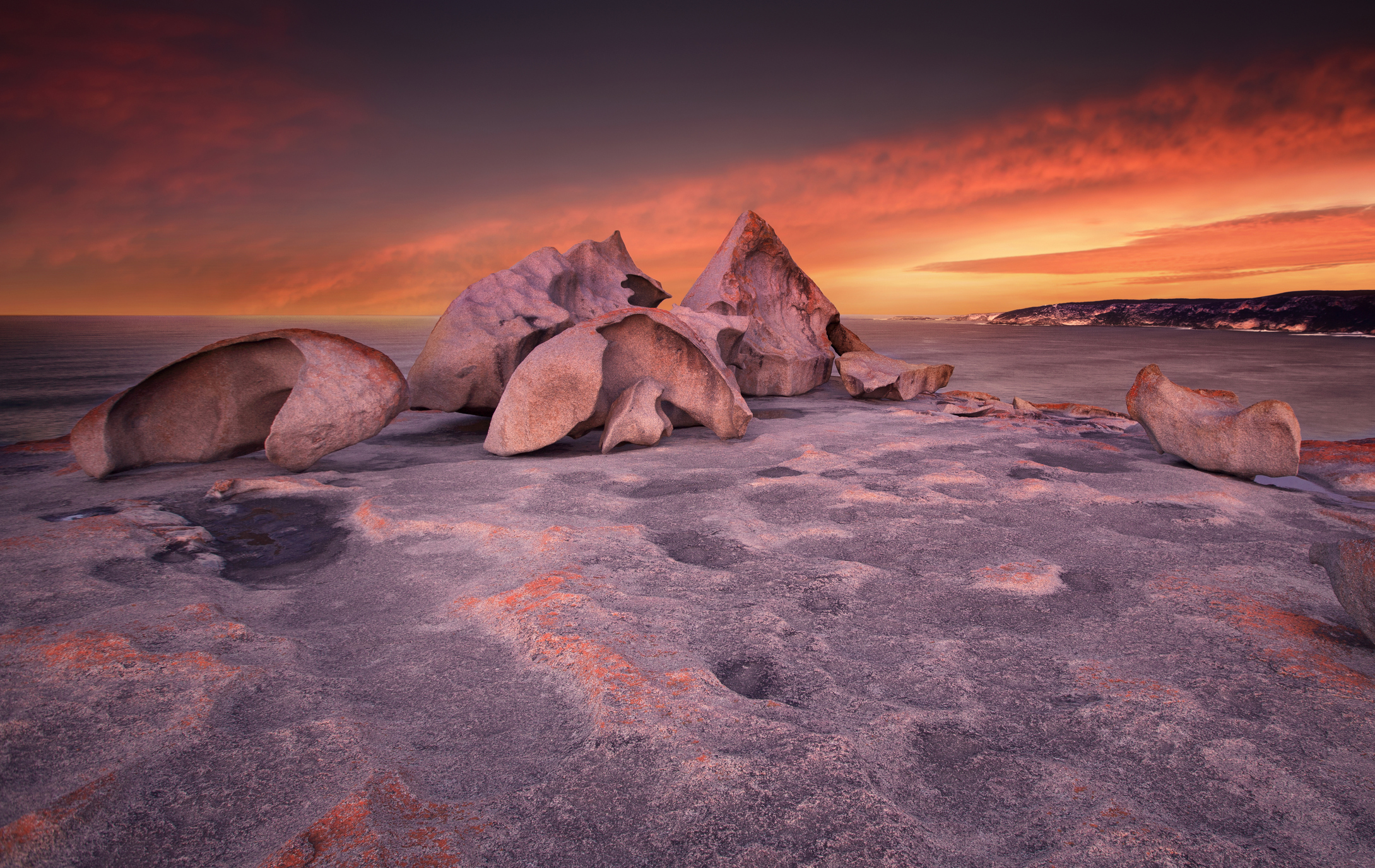 Remarkable Rocks' sculpted granite boulders overlooking the Southern Ocean at sunset, with pink-lit rock surfaces and a glowing orange sky on Kangaroo Island, South Australia.
