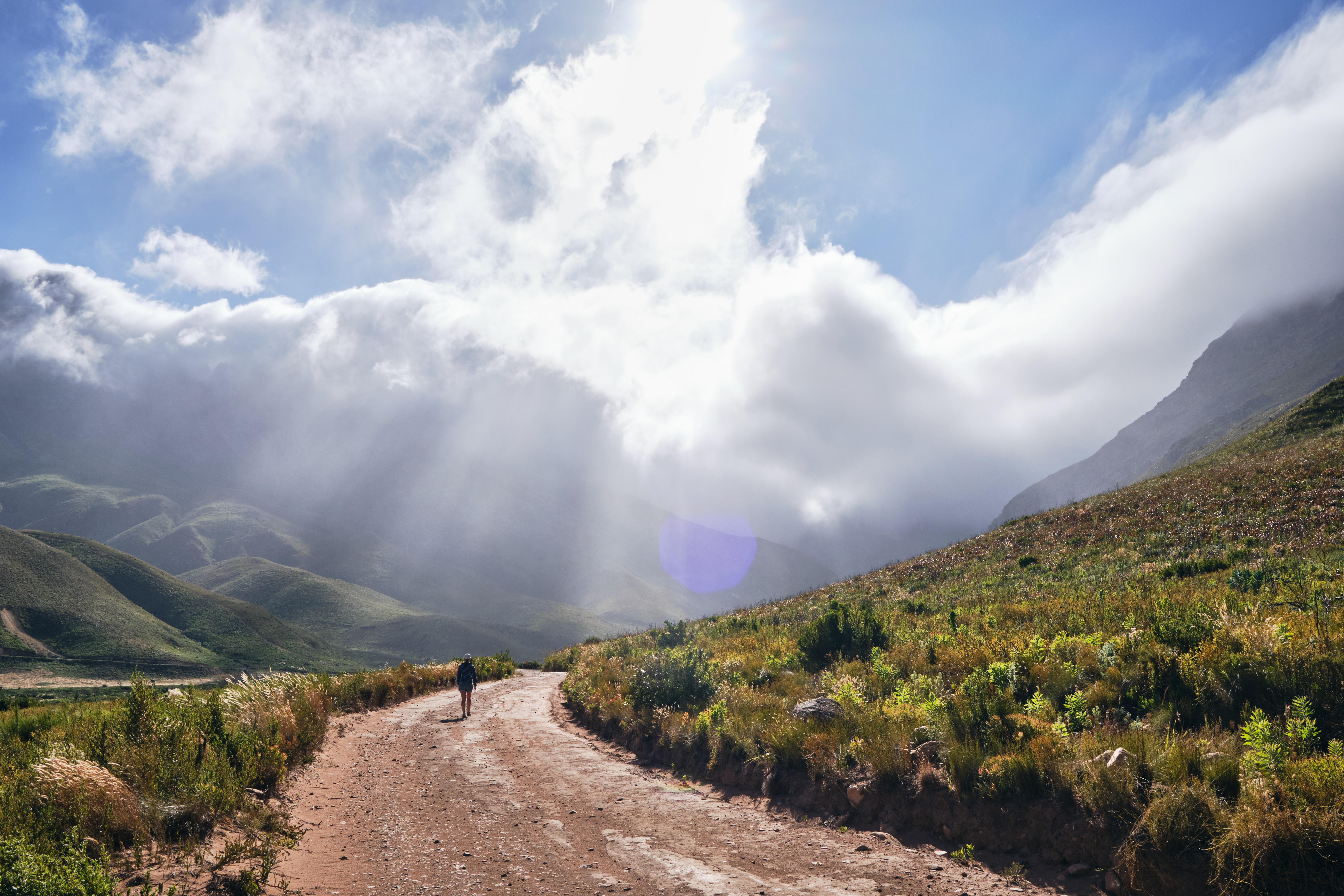 Hiker walking along a dirt road beneath dramatic clouds and sunlight in Jonkershoek Nature Reserve near Stellenbosch, Cape Winelands, South Africa.