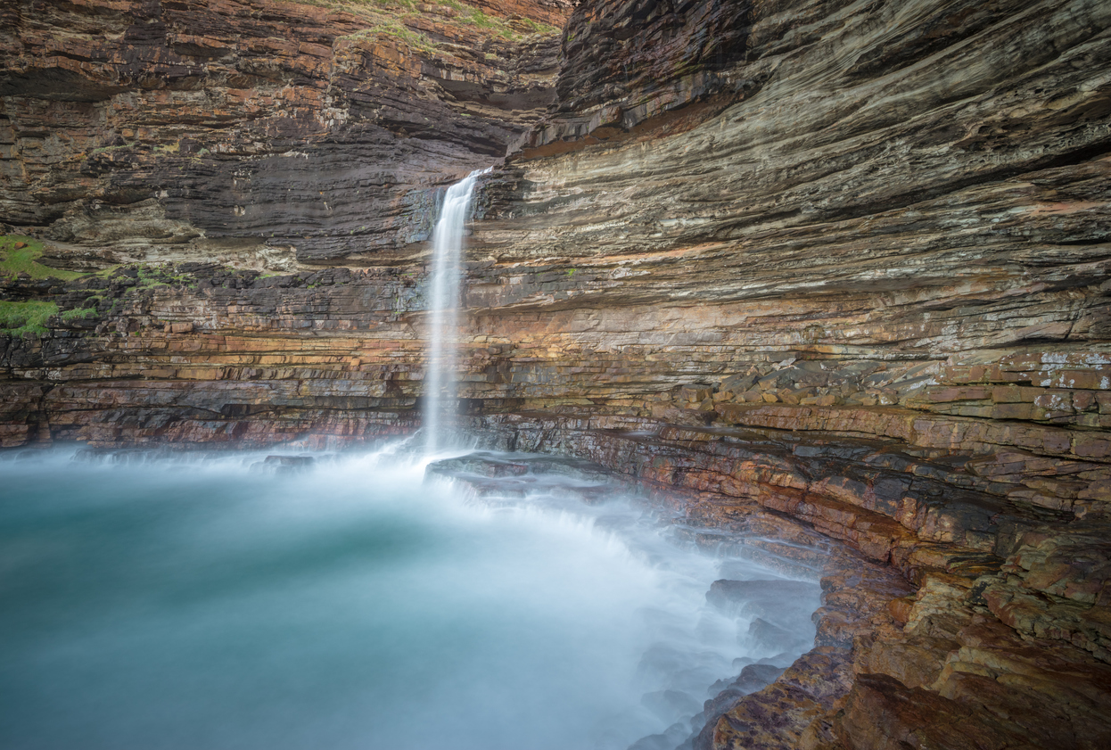 Waterfall Bluff waterfall dropping into a rocky ocean pool beneath towering stratified cliffs on the Wild Coast of the Eastern Cape.