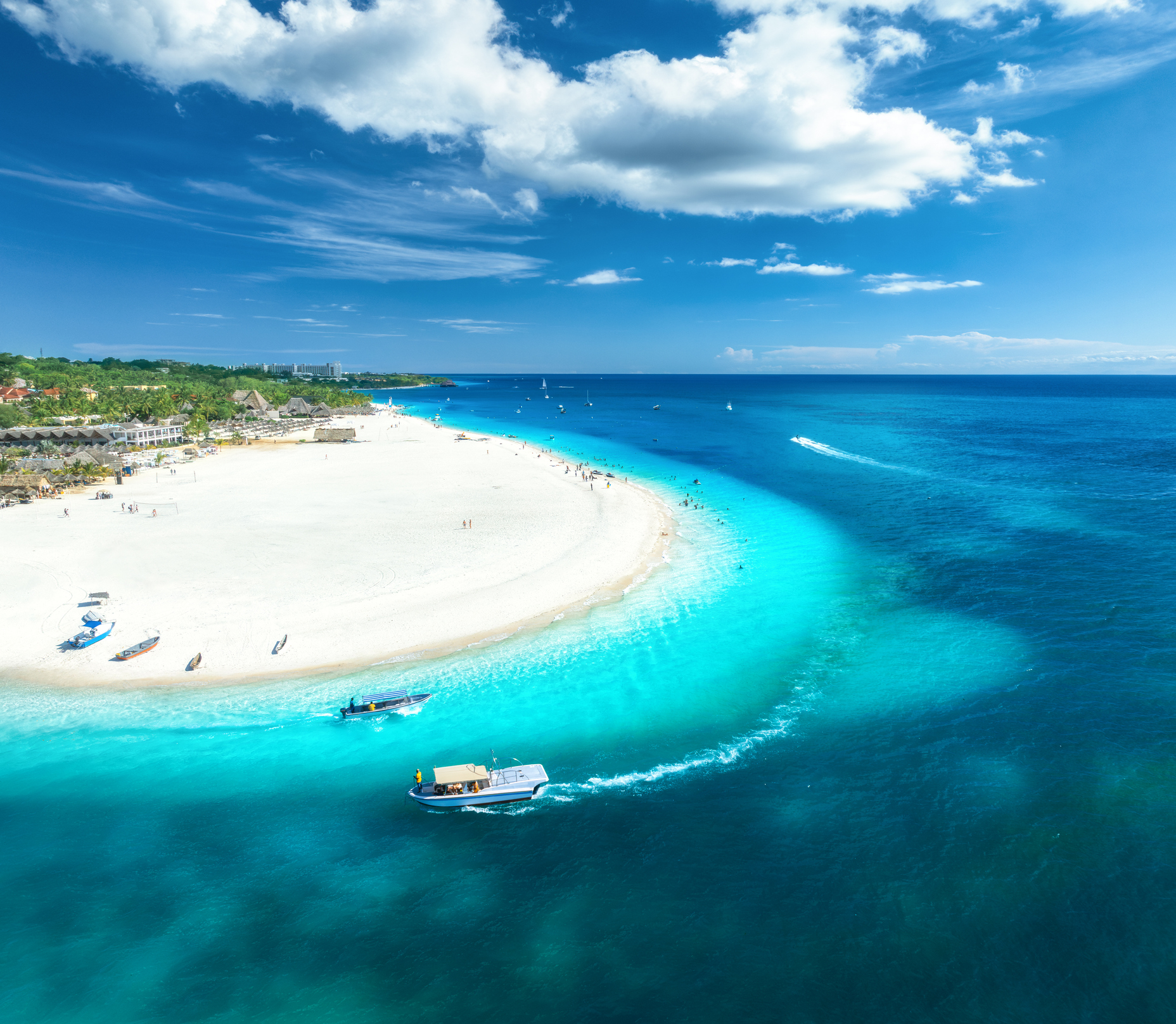 Drone view of Kendwa Beach showing its sweeping crescent of white sand, turquoise shallows and deep blue Indian Ocean on Zanzibar's north coast, Tanzania.