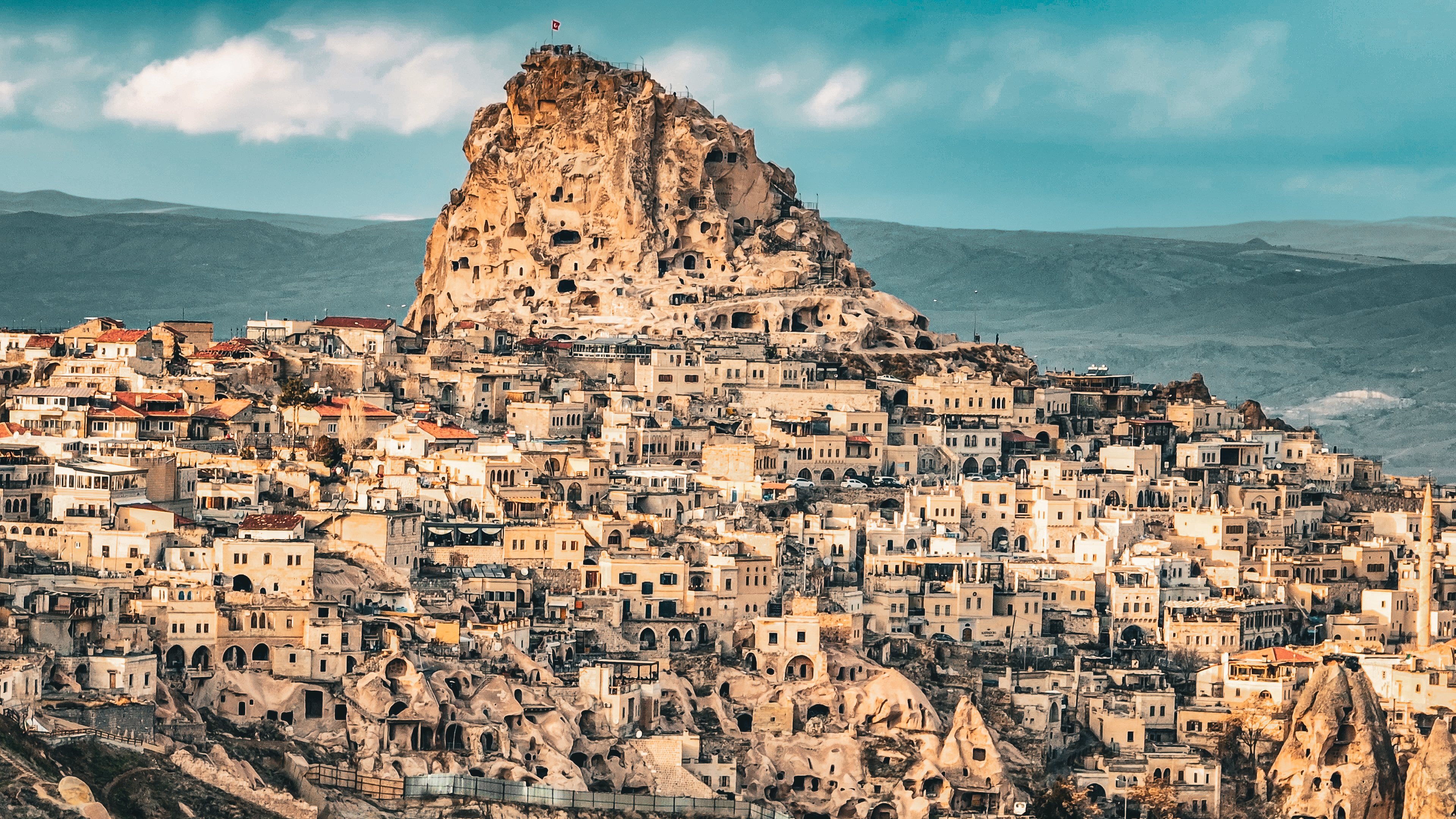 Uçhisar Castle towering above the historic village in Cappadocia, Turkey, with cave dwellings and traditional stone houses surrounding the rock fortress.