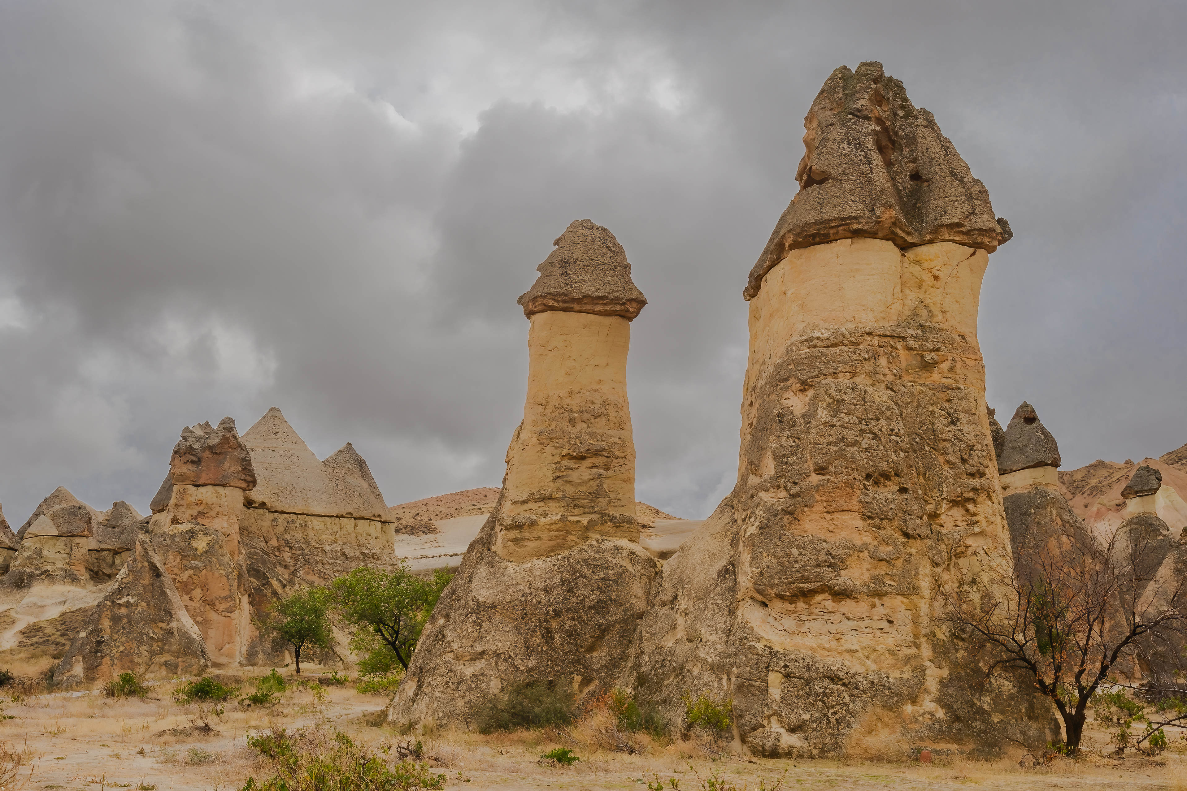 Mushroom-shaped fairy chimneys with dark basalt caps at Paşabağ Fairy Chimneys in Cappadocia, Turkey, beneath dramatic storm clouds.