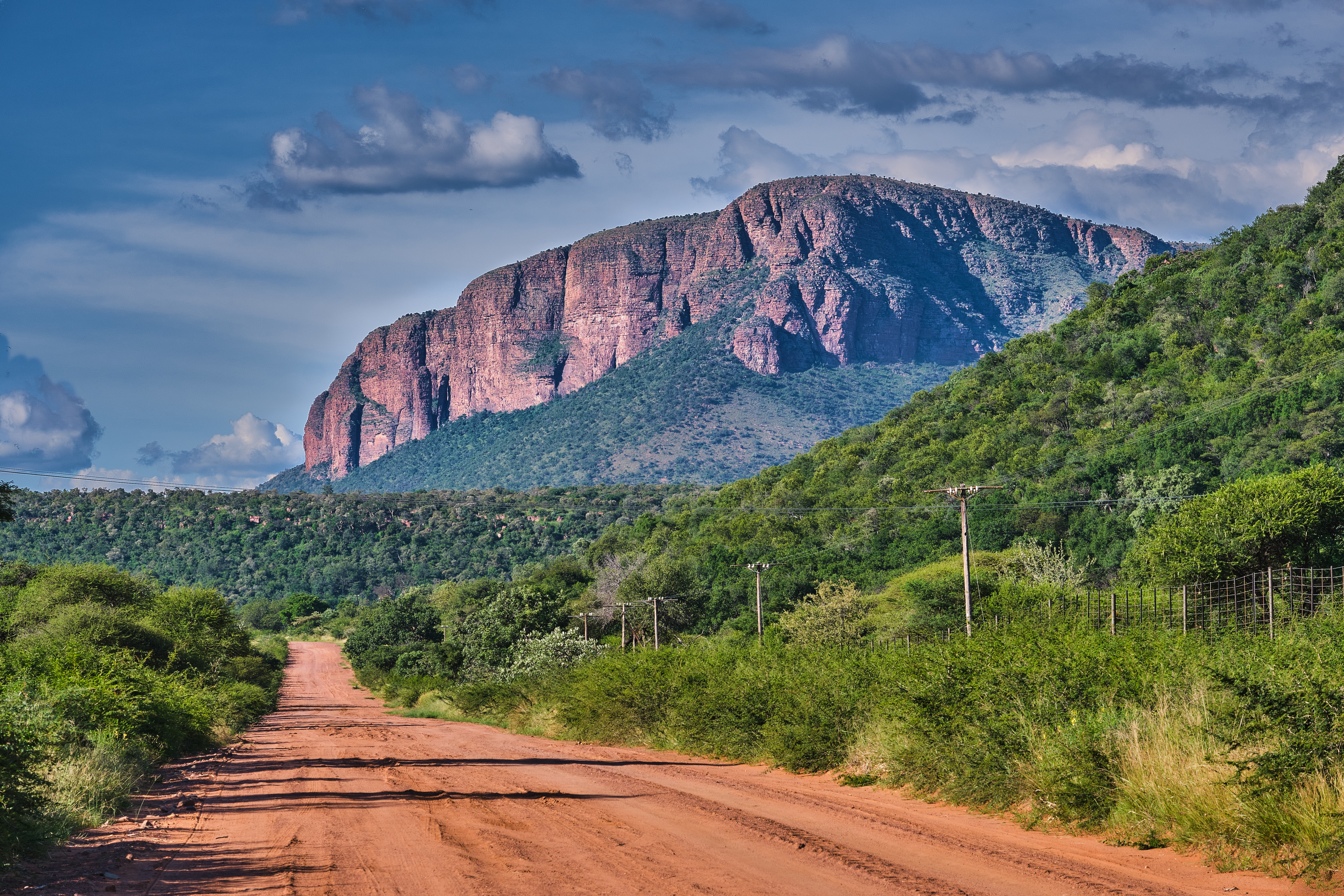 Sunset over a dirt road and bushveld landscape in Marakele National Park, with dramatic cloud formations above the Waterberg mountains in Limpopo, South Africa.