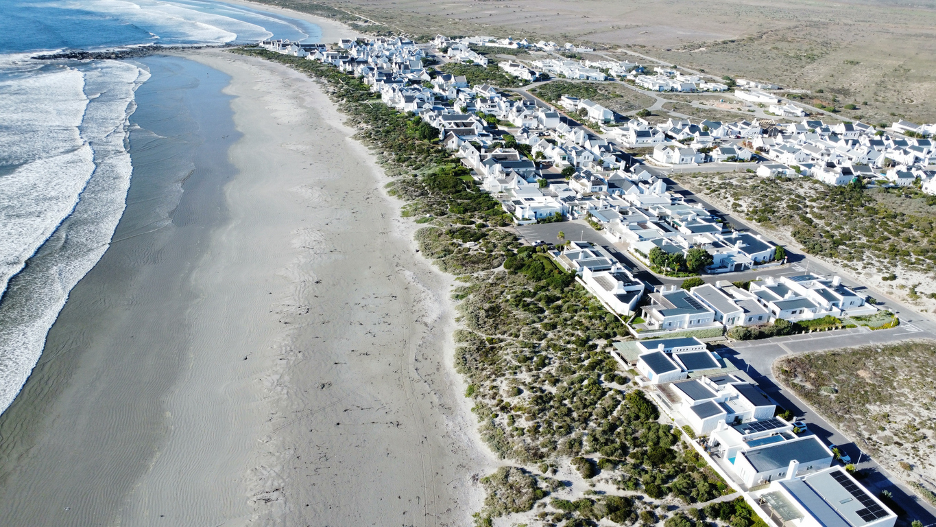 Aerial view of whitewashed houses and beachfront cottages lining the coastline at Paternoster on South Africa’s West Coast, with wide sandy beaches and Atlantic Ocean waves.