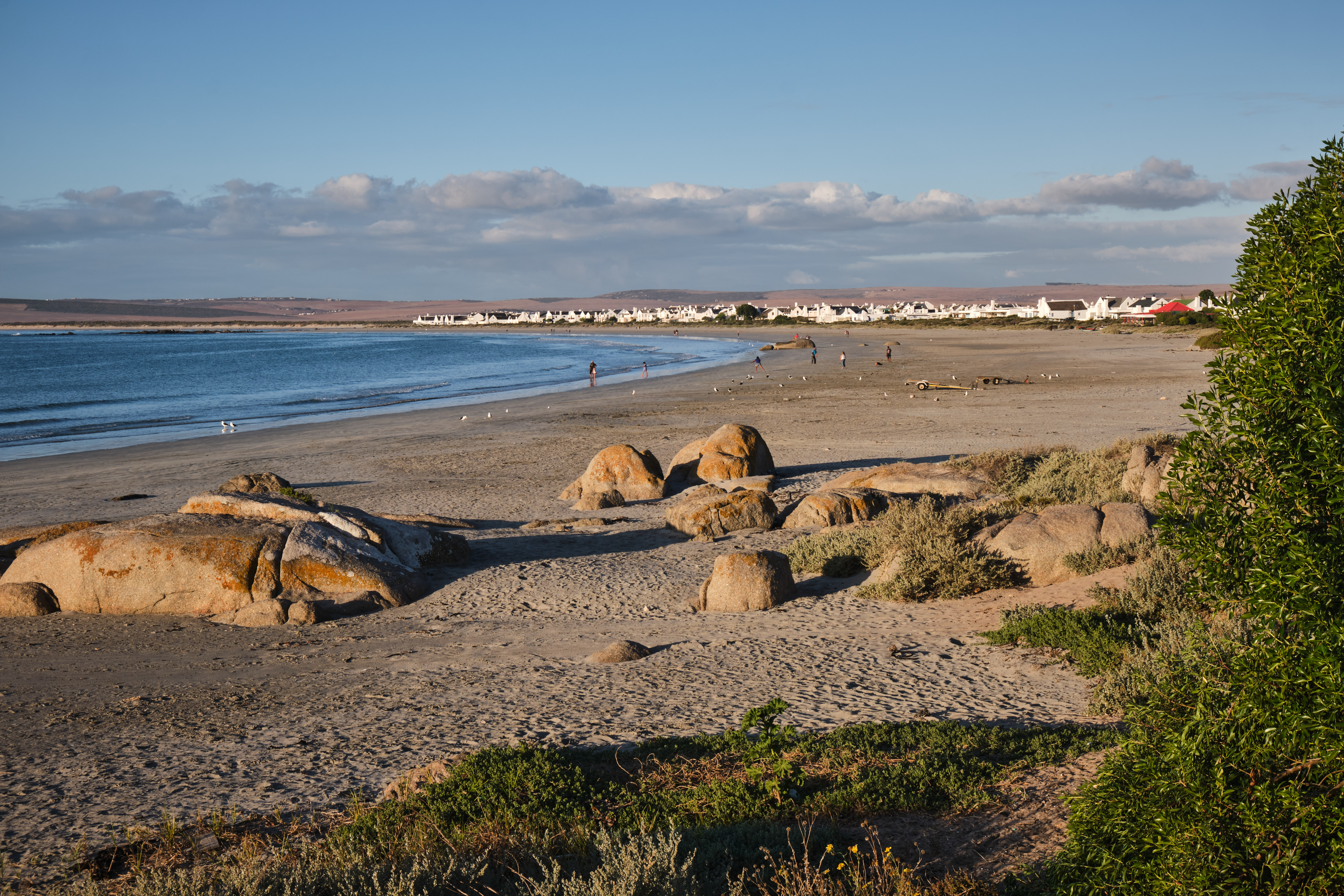Wide beach at Paternoster with granite boulders, calm shoreline and whitewashed village homes in warm evening light.