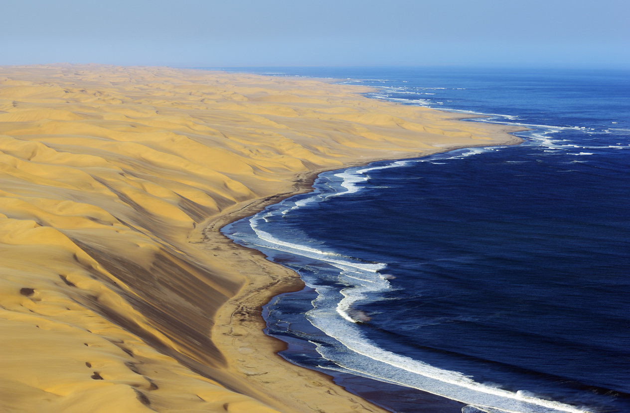 Aerial coastline of large Namib Desert dunes meeting the Atlantic Ocean on Namibia’s Skeleton Coast.