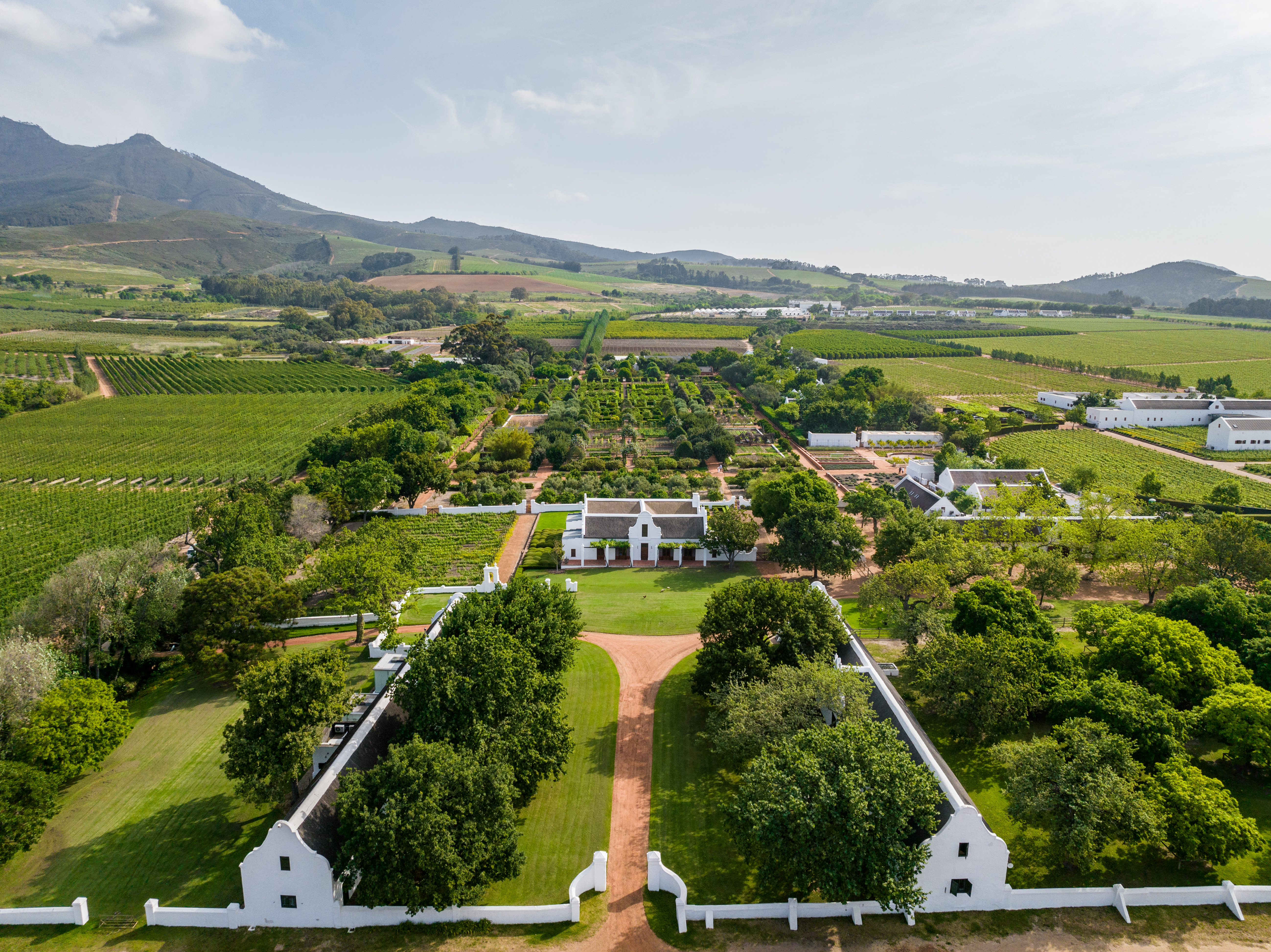 Aerial view of Babylonstoren showing geometric gardens, vineyards, white Cape Dutch farm buildings, and mountain scenery near Franschhoek in South Africa’s Cape Winelands.
