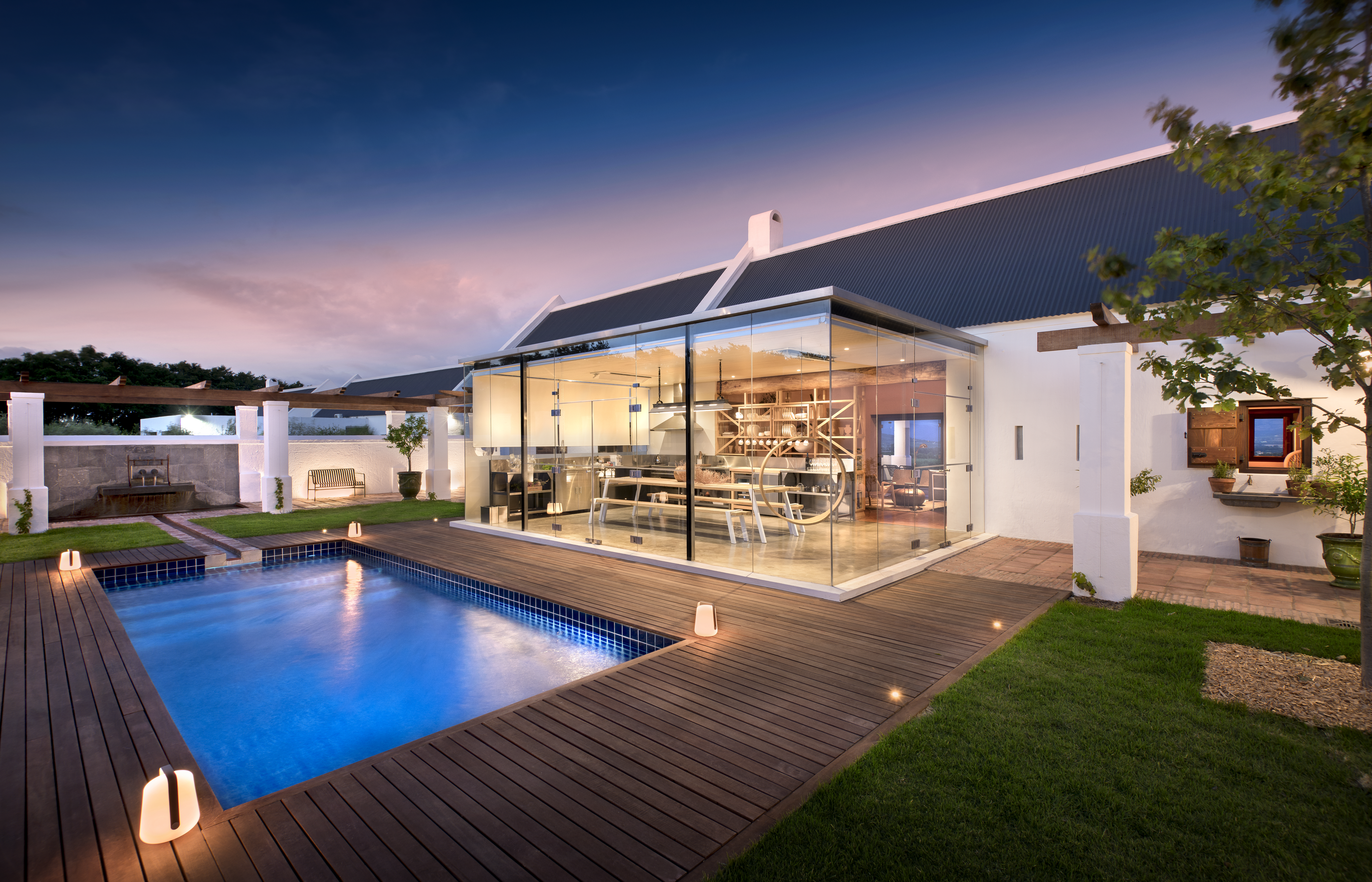 Modern Babylonstoren accommodation with glass architecture, illuminated interiors, swimming pool, and landscaped courtyard at sunset in South Africa’s Cape Winelands.