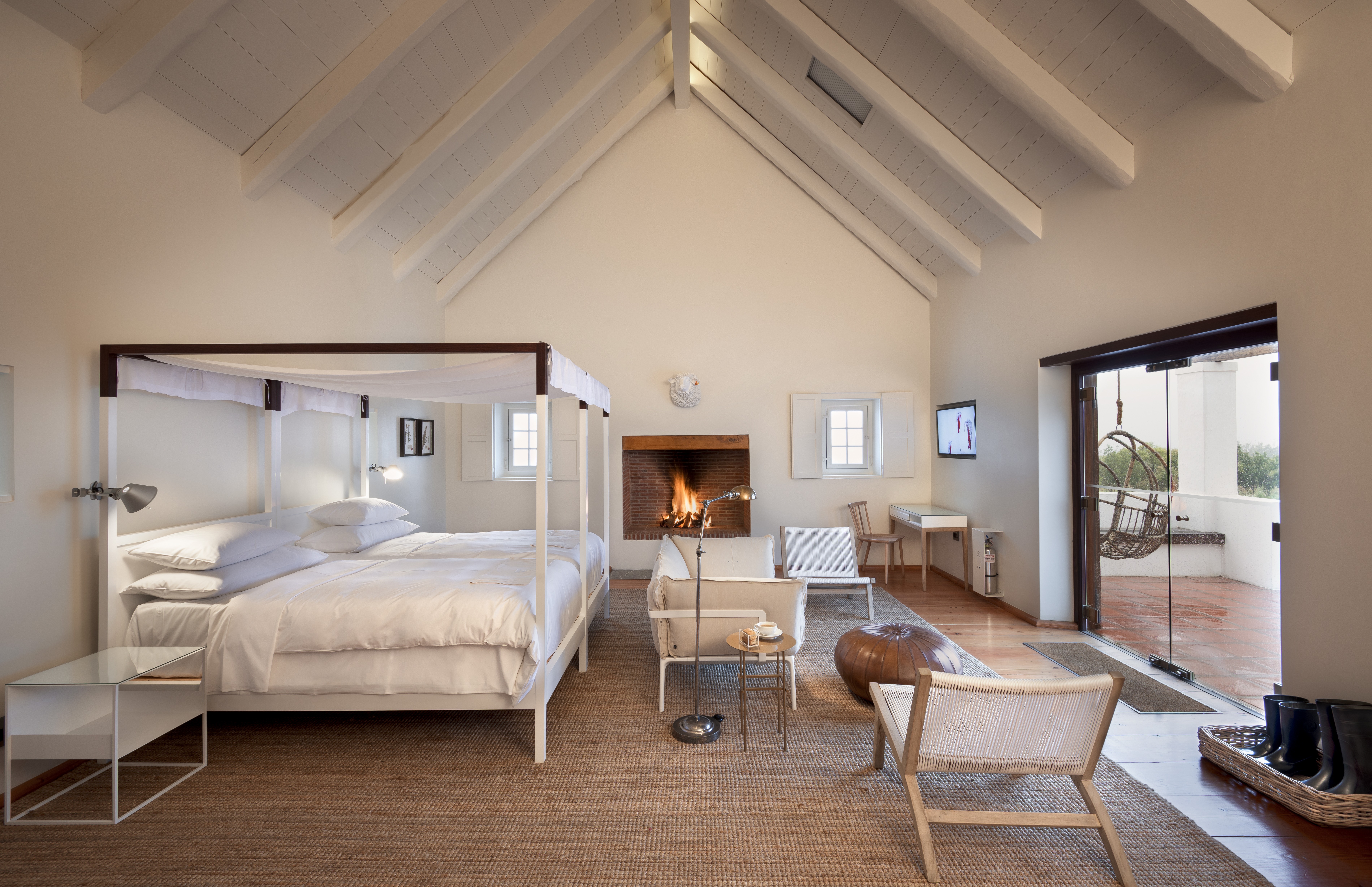 Luxury guest room at Babylonstoren featuring a four-poster bed, vaulted white timber ceiling, fireplace, and terrace access within the Cape Winelands near Franschhoek.