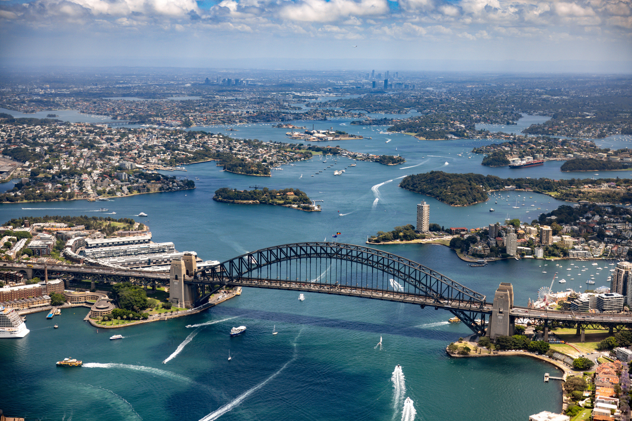 High aerial view across Sydney Harbour with the Harbour Bridge, ferries, islands and waterways stretching towards the western suburbs.