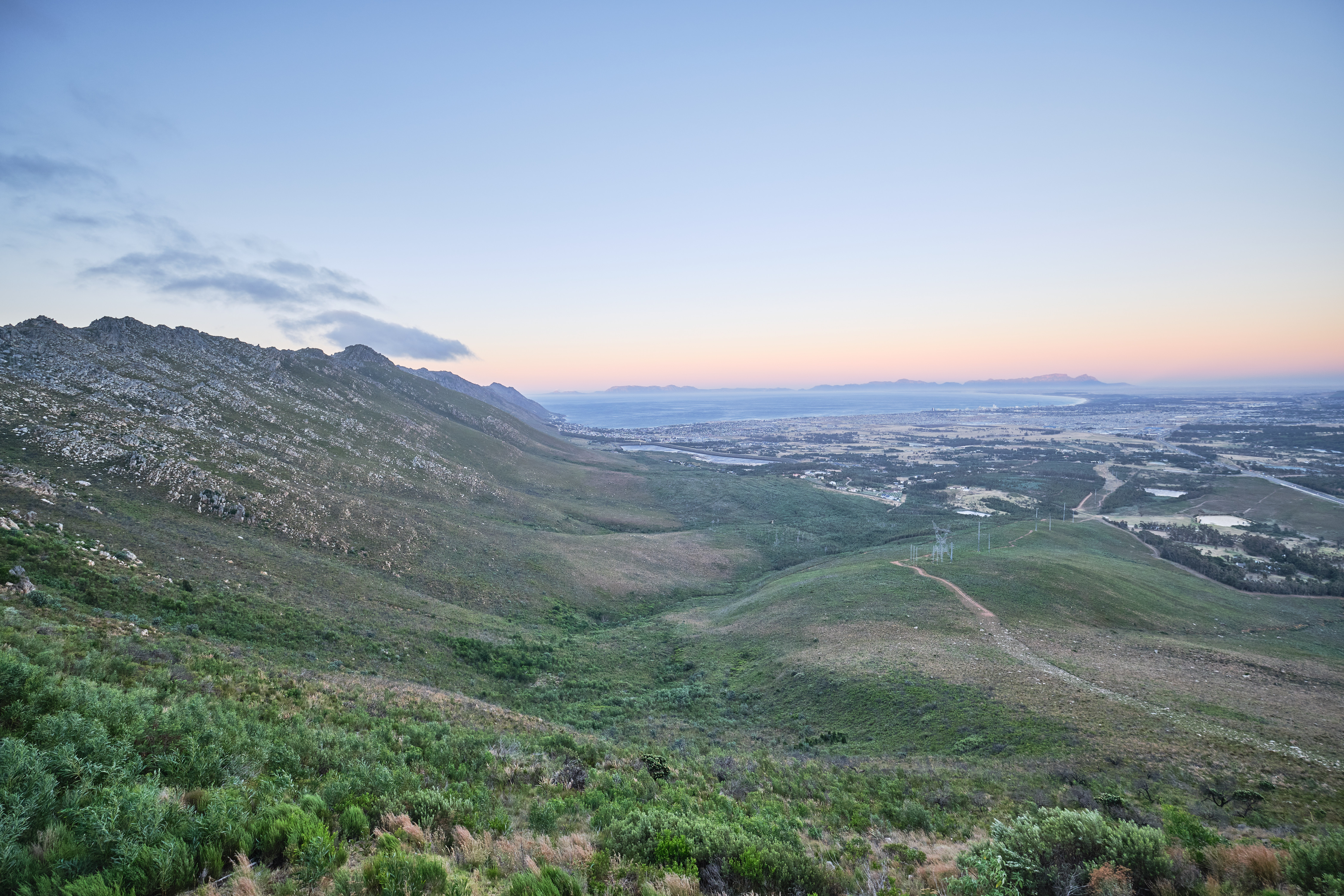 Elevated landscape view from Sir Lowry’s Pass showing green mountain slopes descending toward the Overberg plains in the Western Cape, South Africa.