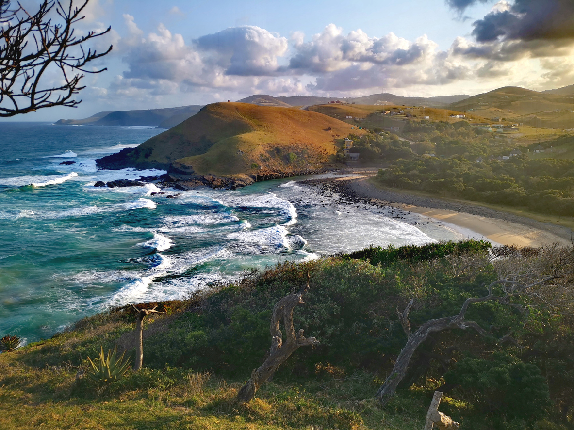 Elevated view of Coffee Bay coastline with waves, rocky shoreline, grassy headlands and scattered rural settlements on the Wild Coast.