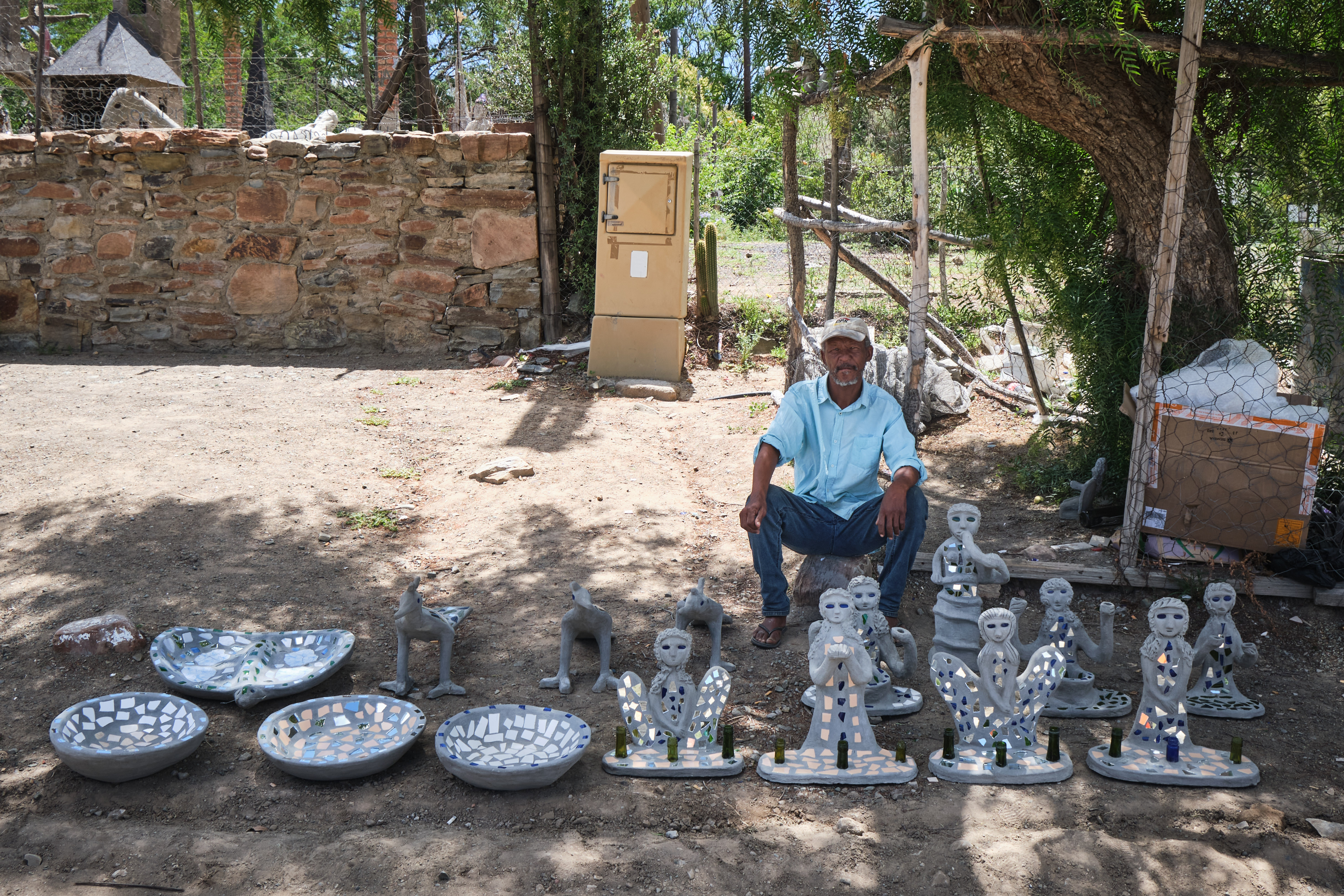 Local artisan displaying handmade mosaic sculptures and decorative artworks in Nieu-Bethesda, Eastern Cape, South Africa.