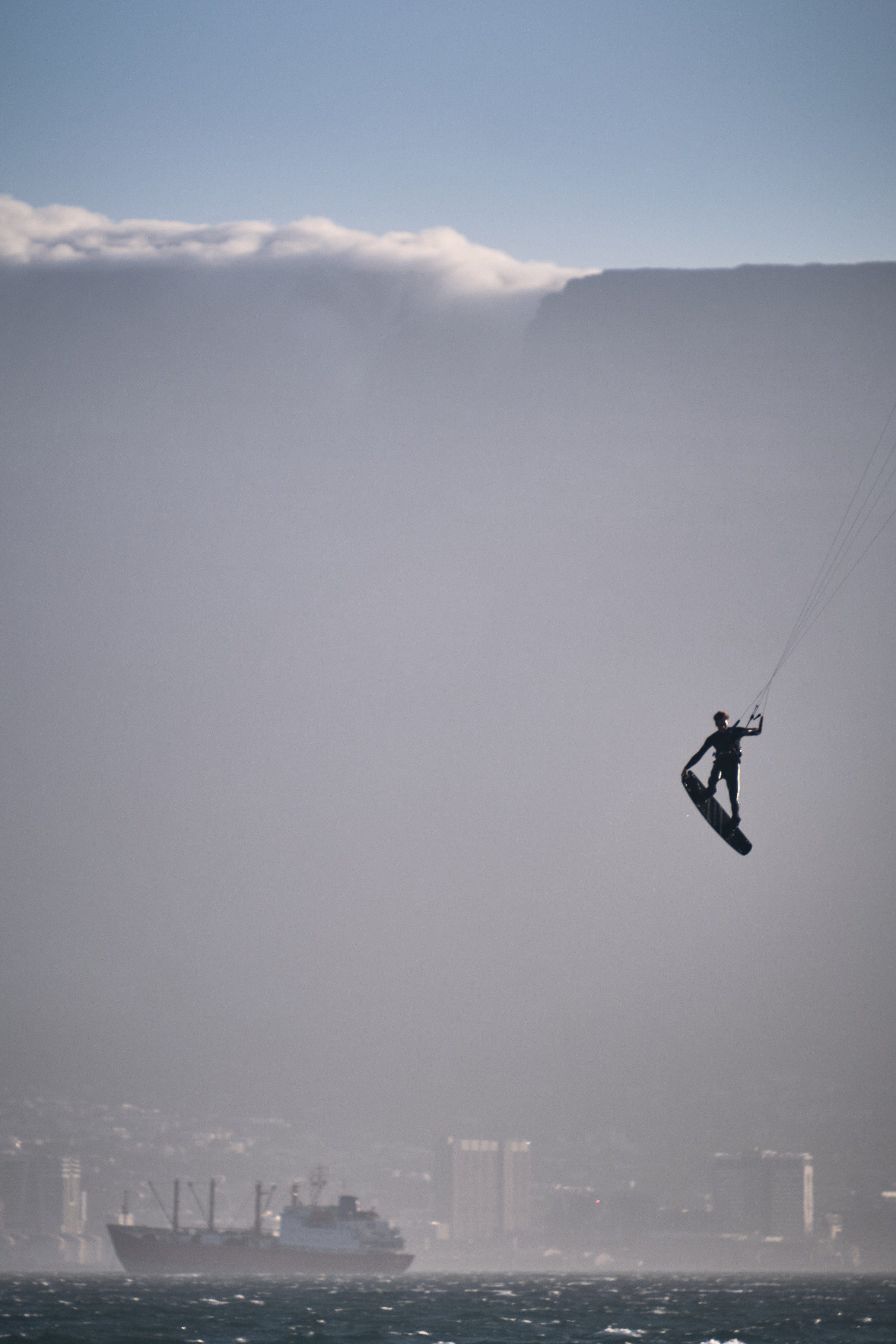 Kite surfer performing a jump at Bloubergstrand with Table Mountain and tablecloth cloud in the background across Table Bay in Cape Town.