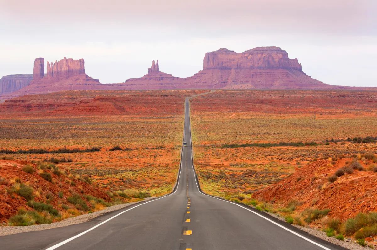 Straight highway leading toward sandstone buttes across Monument Valley in the Southwest United States.