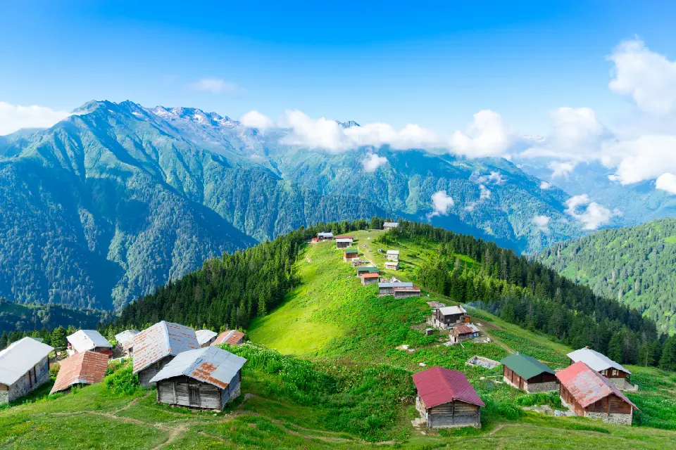 Traditional wooden houses on Pokut Plateau with green slopes and the Kaçkar Mountains rising behind, near Çamlıhemşin, Rize, Turkey.