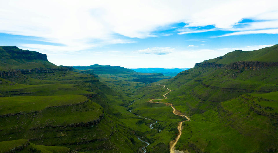 Aerial view of the Sani Pass valley with a winding mountain road, river and steep green escarpment slopes in the Drakensberg between South Africa and Lesotho.
