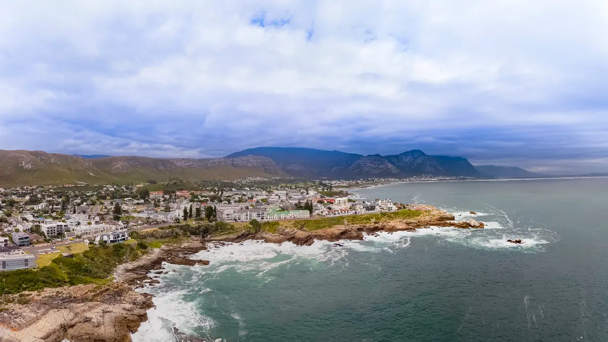 Coastal aerial panorama of Hermanus with rocky shoreline, ocean cliffs, and mountains along the Whale Coast in South Africa.