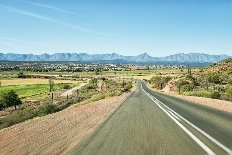 Road leading toward Oudtshoorn across semi-arid farmland with the Swartberg Mountains in the Little Karoo, South Africa