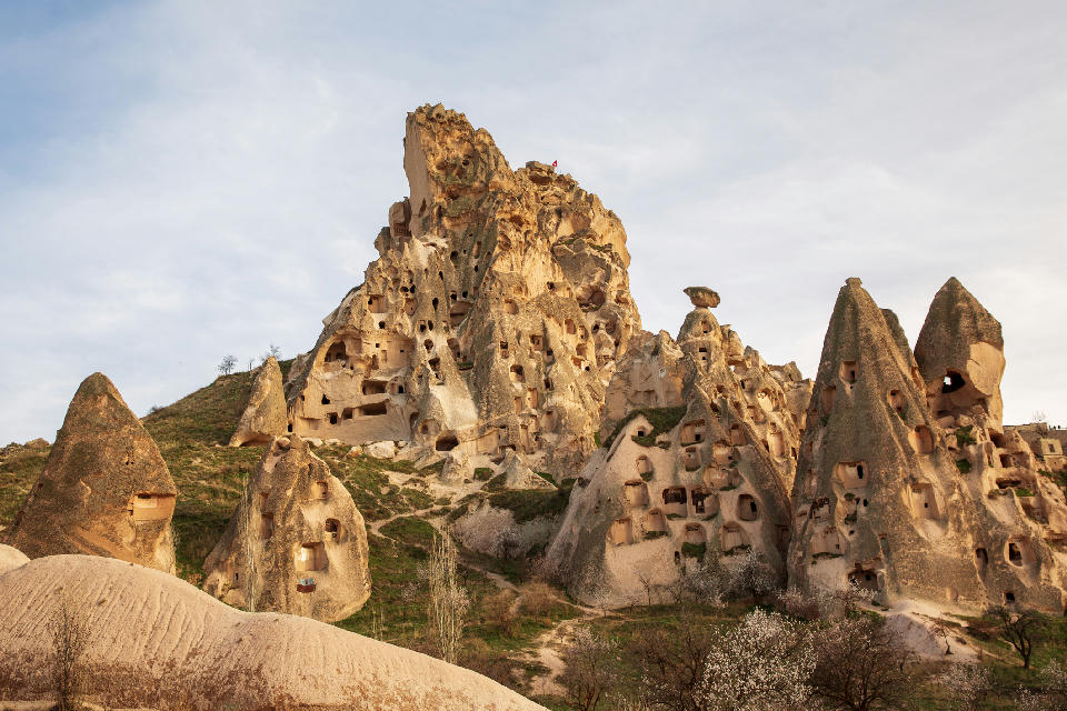 Uçhisar Castle surrounded by tall fairy chimneys and rock-cut cave dwellings in Cappadocia, Turkey.