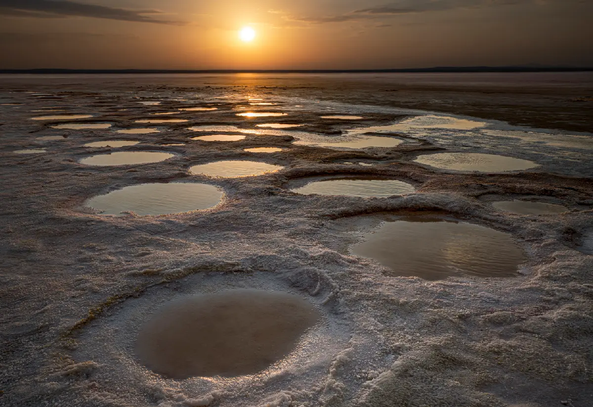 Sunset reflecting in shallow pools surrounded by white salt formations at Lake Tuz, Turkey.