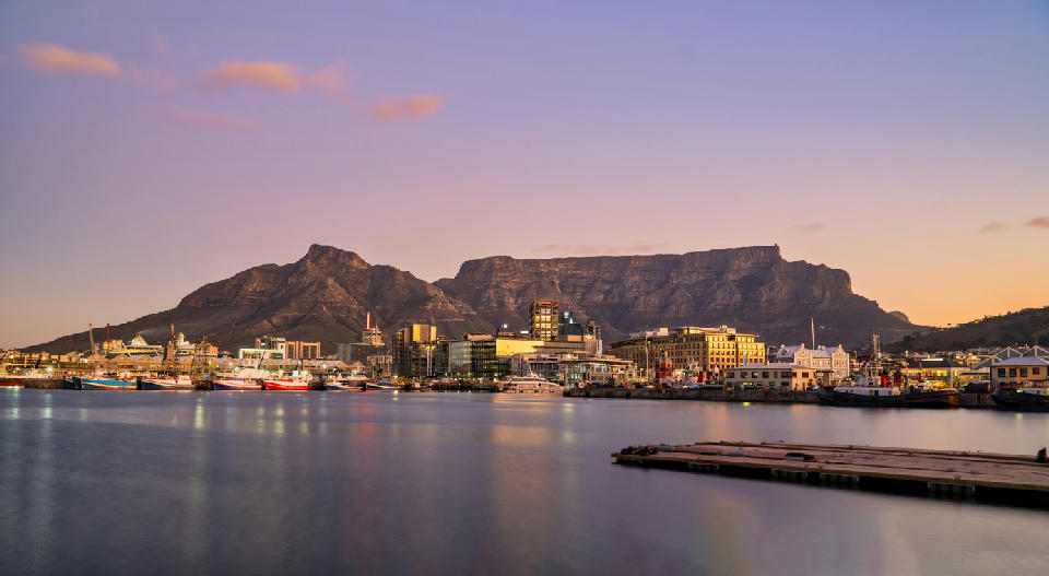 V&A Waterfront harbour at sunset with Table Mountain forming a flat-topped backdrop above Cape Town, South Africa.