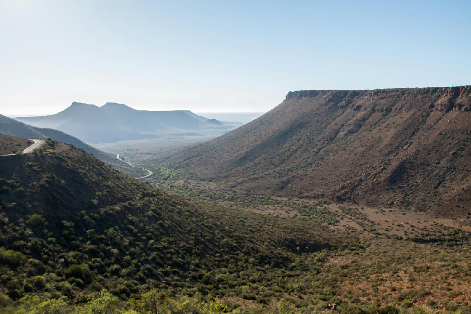 Wide view of a mountain pass in Karoo National Park with steep escarpments, a winding road, and expansive semi-desert valleys under clear skies in South Africa.