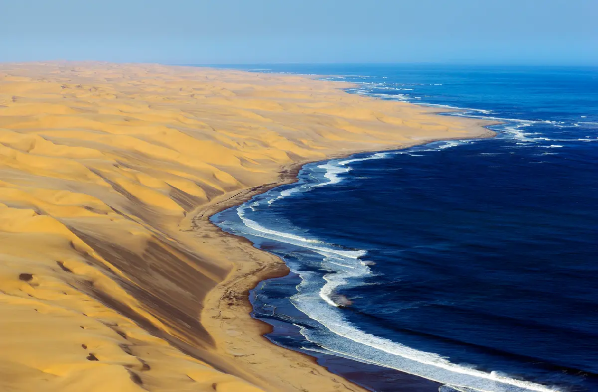 Aerial coastline of large Namib Desert dunes meeting the Atlantic Ocean on Namibia’s Skeleton Coast.