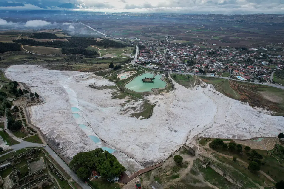 Aerial view of Pamukkale, Turkey, showing the white travertine terraces, turquoise pools, nearby Hierapolis ruins and the town and countryside beyond.