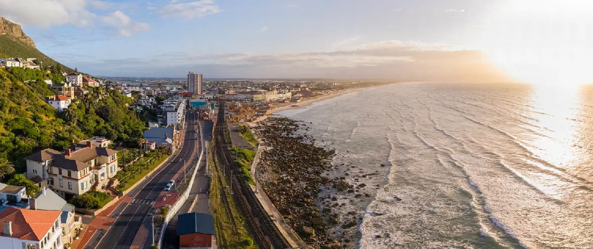 Aerial view of Muizenberg Beach on False Bay with railway, coastal road, and long sandy shoreline at sunrise in Cape Town, South Africa.