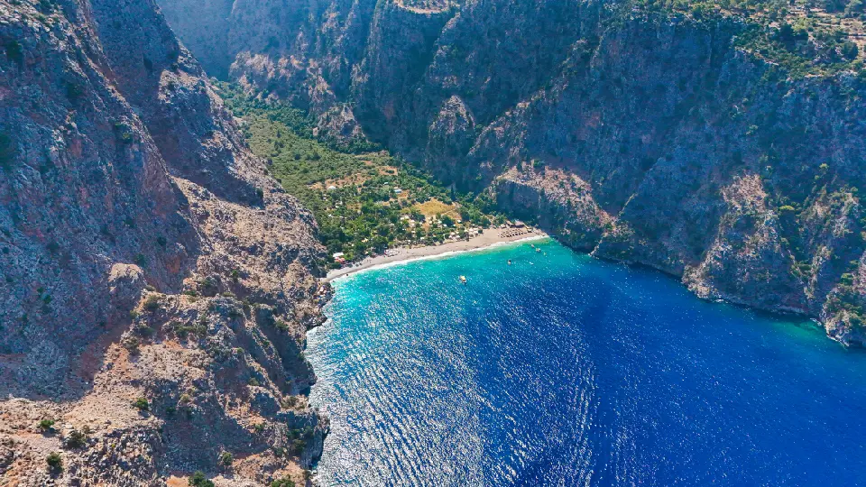 Aerial view of Butterfly Valley near Ölüdeniz, with a turquoise Mediterranean bay, beach, and steep rocky cliffs in Fethiye, Turkey.