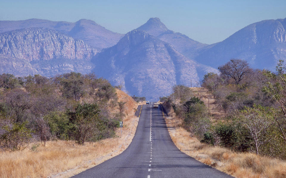 Two-lane road running through dry bushveld towards the rugged cliffs and peaks of Abel Erasmus Pass in Limpopo Province, South Africa.