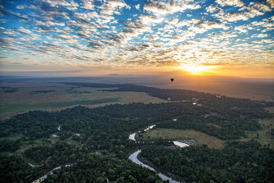 Hot air balloons flying above the Mara River and northern Serengeti landscape at sunrise in Tanzania.