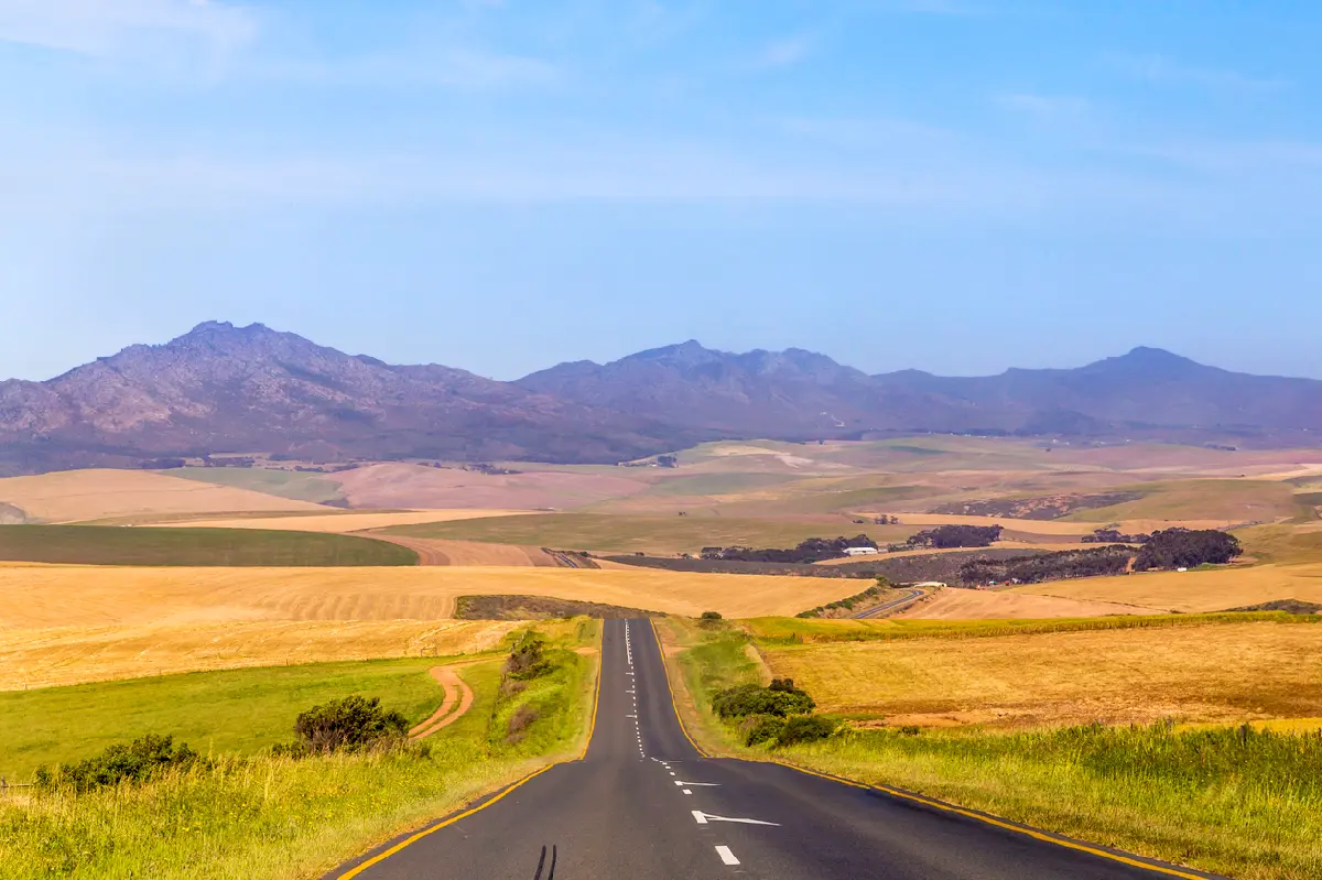 Long road through rolling farmland and mountain landscapes near Stanford in the Overberg region of the Western Cape, South Africa.
