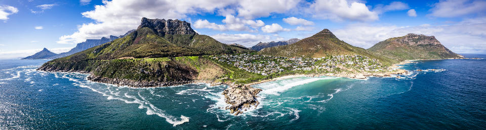 Aerial view of Llandudno Beach showing a sheltered sandy cove, granite boulders, and steep mountain slopes along the Atlantic Seaboard in Cape Town.
