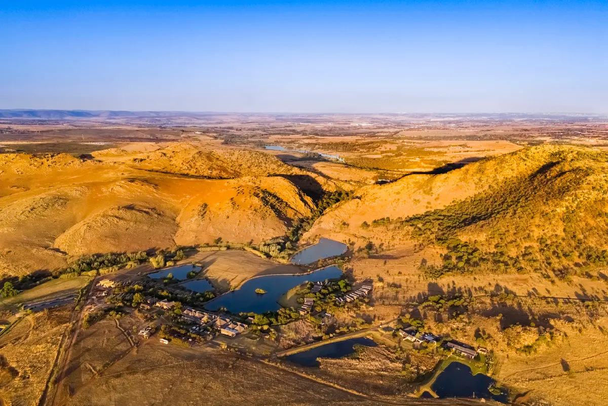 Aerial view of the Cradle of Humankind showing rugged hills, open countryside and small lakes surrounded by golden grasslands in Gauteng, South Africa.