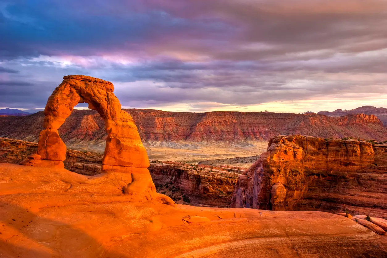 Delicate Arch silhouetted against a sunset sky above desert canyon in Arches National Park Utah