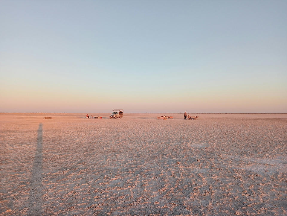 Sunset over the vast white salt flats of Makgadikgadi Pans in Botswana with a safari vehicle on the horizon.