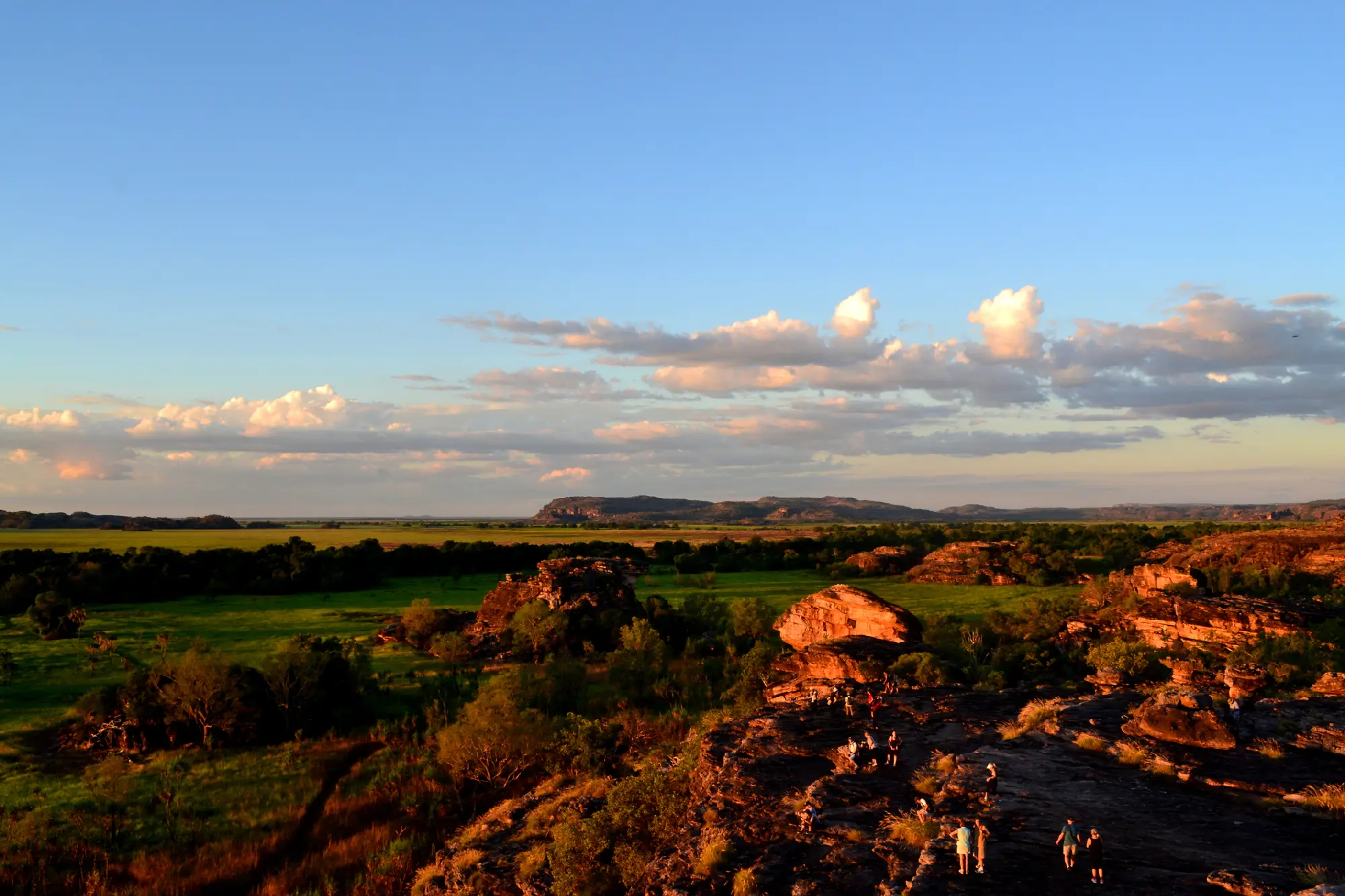 Visitors standing on sandstone outcrops at Ubirr overlooking green floodplains and distant escarpments in Kakadu National Park, Northern Territory, Australia.