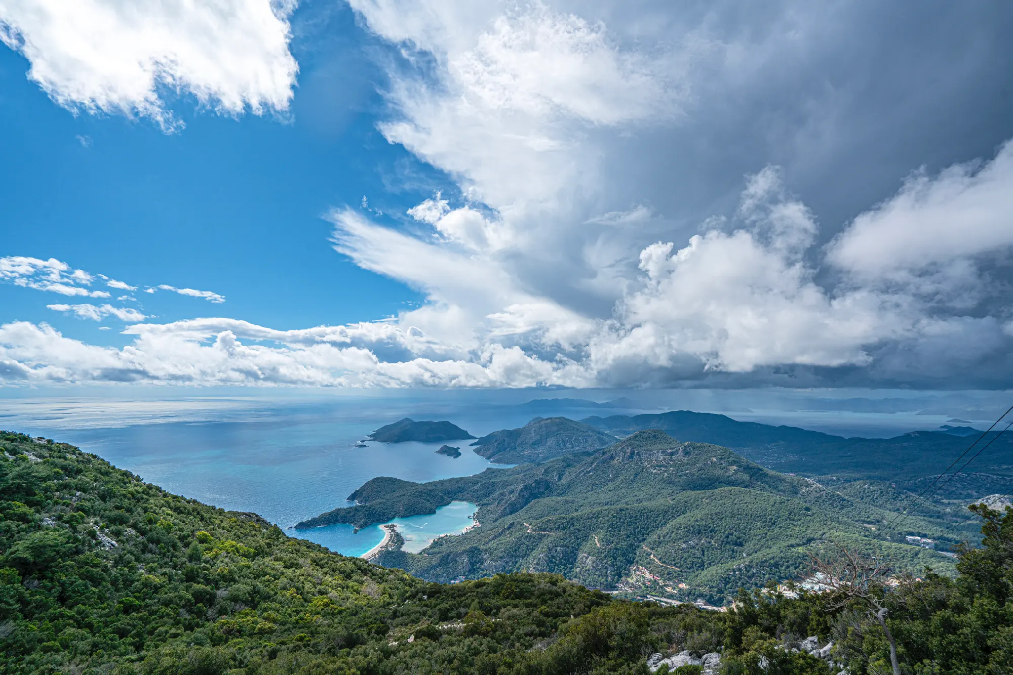 Panoramic view from Babadağ across forested mountains, the Blue Lagoon and Mediterranean coastline near Ölüdeniz, Türkiye.