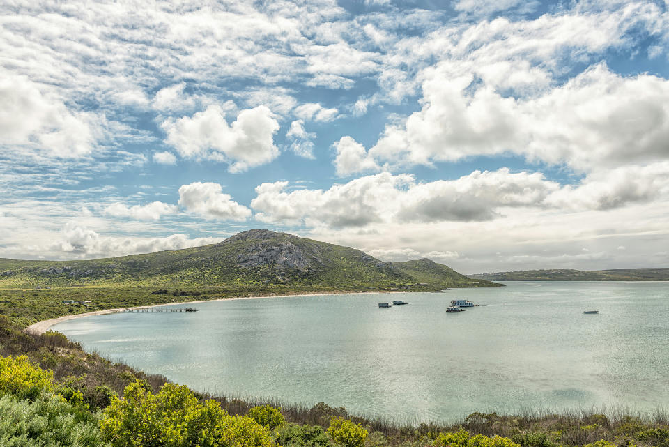 Panoramic view of Kraalbaai on Langebaan Lagoon with houseboats, jetty and granite hills in West Coast National Park, South Africa.