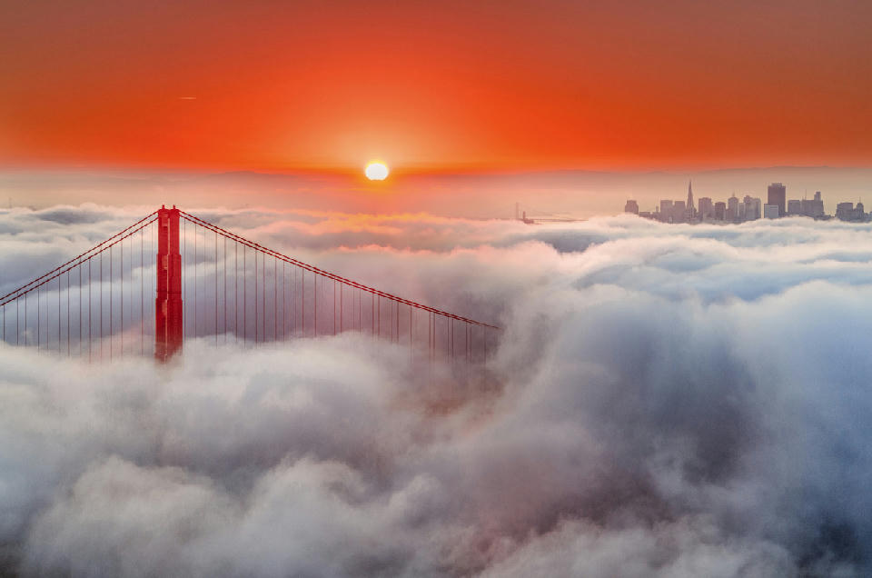 Golden Gate Bridge emerging above fog at sunrise with San Francisco skyline in background