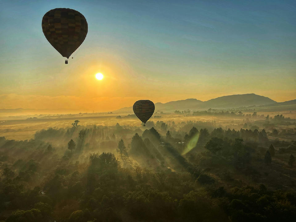 Hot-air balloons floating above the misty Magaliesberg valley at sunrise near Hartbeespoort, South Africa.