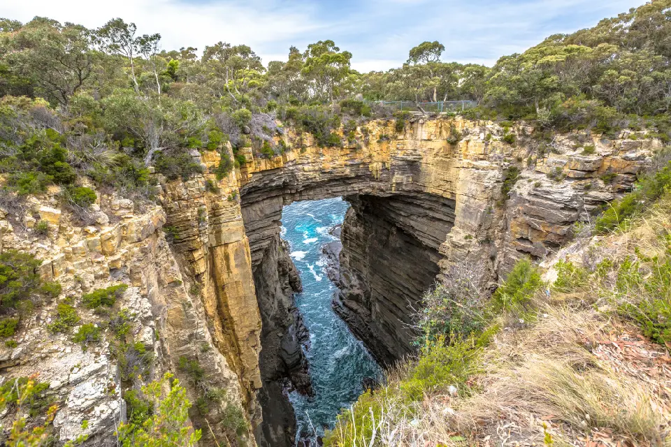 Wide view of Tasman Arch forming a natural rock bridge above a deep ocean channel on the Tasman Peninsula, Tasmania.
